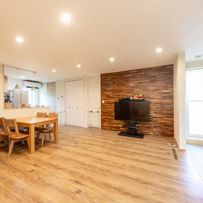 リビングは天然木の質感を生かしたウッドパネルがお洒落な空間を演出。収納と個室エリアへと続くドアは目立たないように壁と同じ白をセレクト。ライフスタイルの変化に合わせて移動できるようにテレビはスタンドタイプにしている。土間の突き当たりには庭に直接出られるドアを配した。