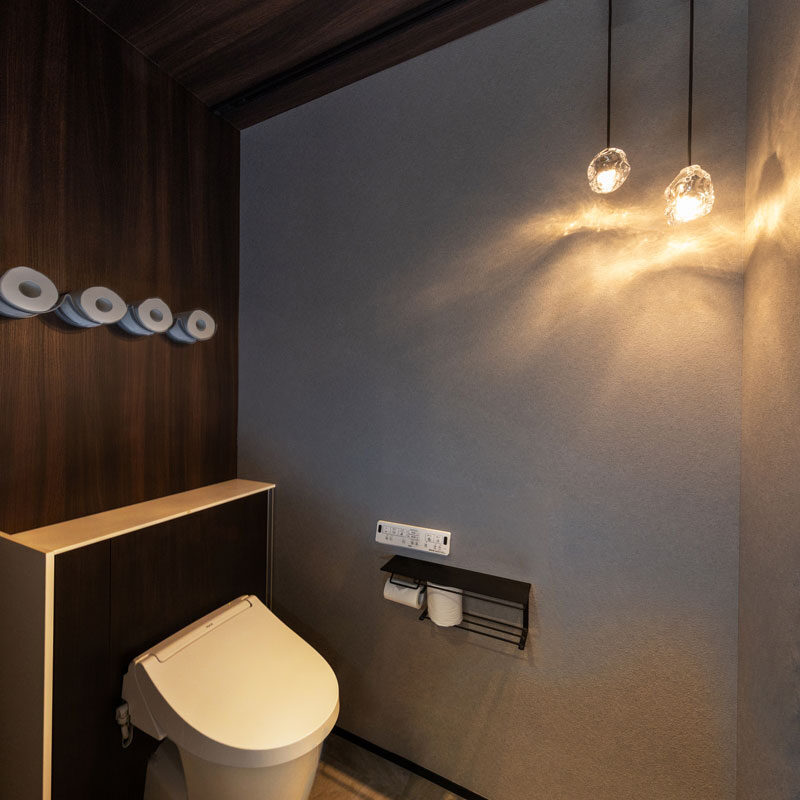 混み合う朝のことを考えて、「トイレは絶対に２つ欲しかった」と奥様。ホール付近に設けられたトイレで、壁のペーパーホルダーや、あえて片側に寄せた照明がおしゃれ。実はこちらタンクレス風のトイレで、背面のタンク部分を収納で隠した既製品。