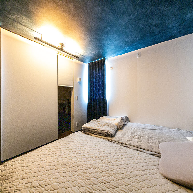 家の一番奥まったところにある主寝室は、夜空のような天井クロスと間接照明がムーディー。ロールスクリーンで仕切られた向こうの一角は、写真右のウォークインクローゼット兼床下エアコンの設置場所になっている。