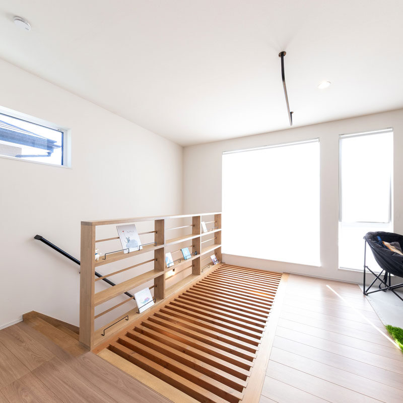 冷気・暖気の通り道である格子床は、ご一家にとっては憩いの場でもある。布団を敷いて寝転び、高窓から空を眺めたりすることも。ホールの開放感を高めるため、吹き抜け腰壁を柵状にして絵本棚として活用。すっきりとして格子床と一体感がある。